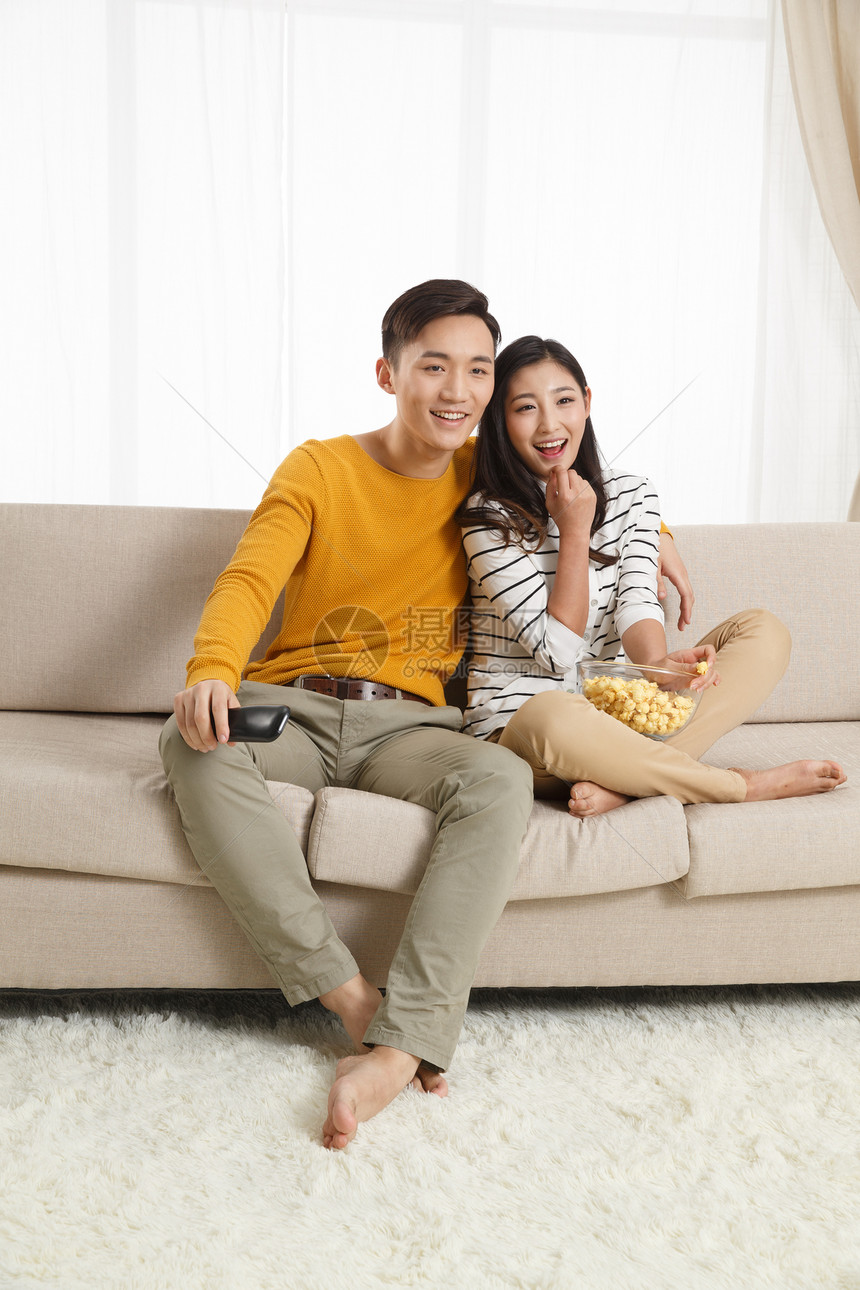 20多岁东亚青年情侣坐着沙发上看电视图片
