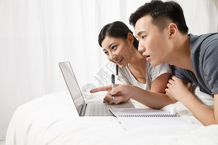亚洲人夫妇青年夫妇青年情侣趴在床上看电脑图片