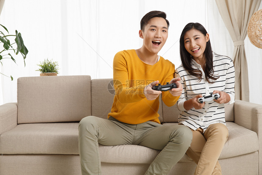 欢乐20到24岁东亚青年情侣坐着沙发上玩游戏图片