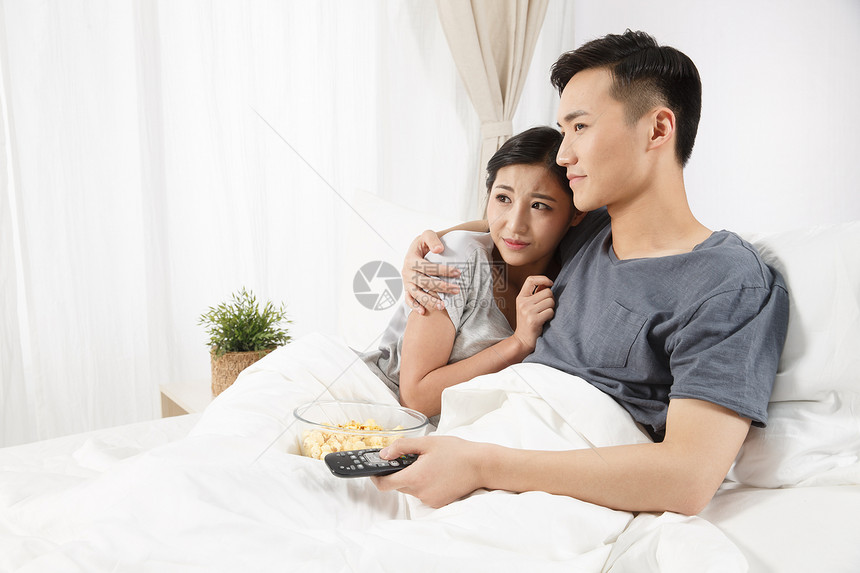 白昼斜靠水平构图青年情侣坐着床上看电视图片