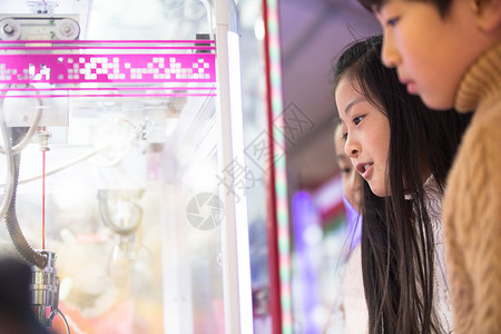 小学生玩游戏机小学生毛绒玩具诱惑男孩女孩在游戏厅玩耍背景