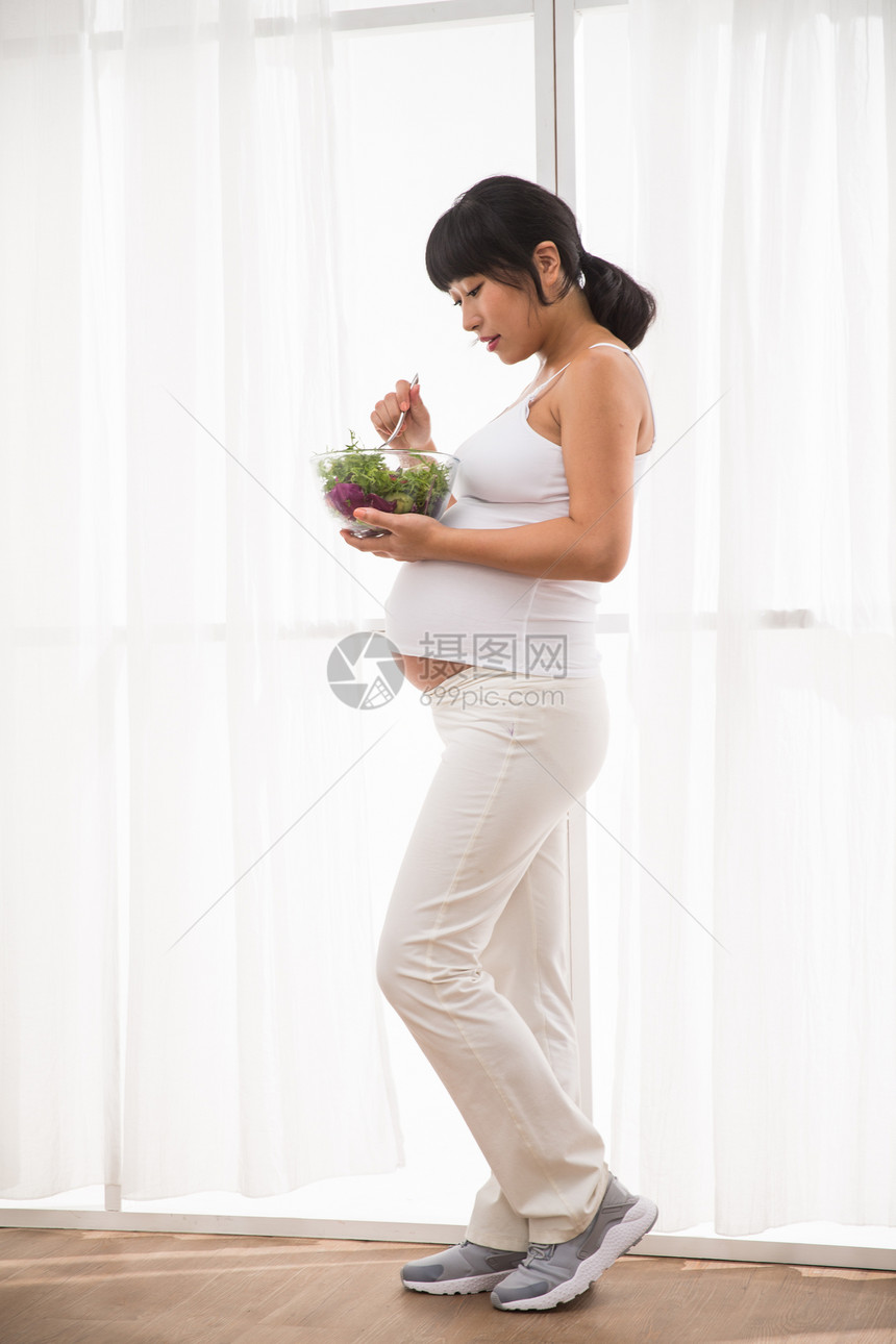 保护成年人人幸福的孕妇吃蔬菜沙拉图片