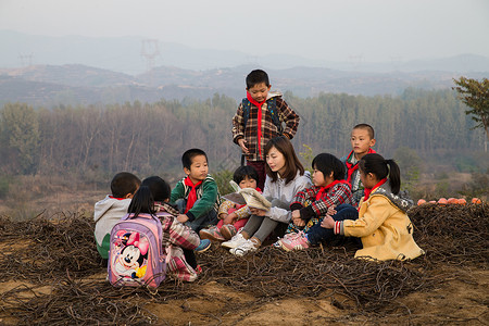 坐着看书的男孩坐着山亚洲乡村教师和小学生在户外学习背景