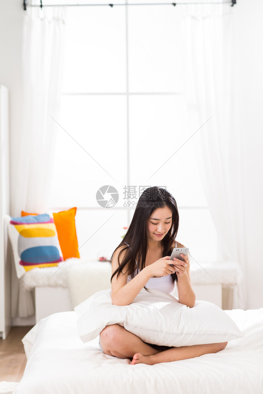 大半身发短信舒适青年女人在卧室用手机图片