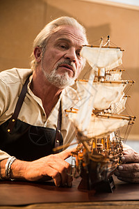 现代工作台休闲装老年男人在制作帆船模型高清图片