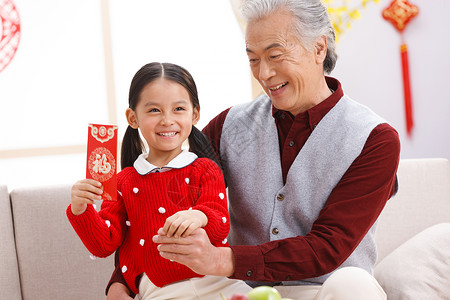 抱红包坐着微笑户内小女孩和爷爷过新年背景