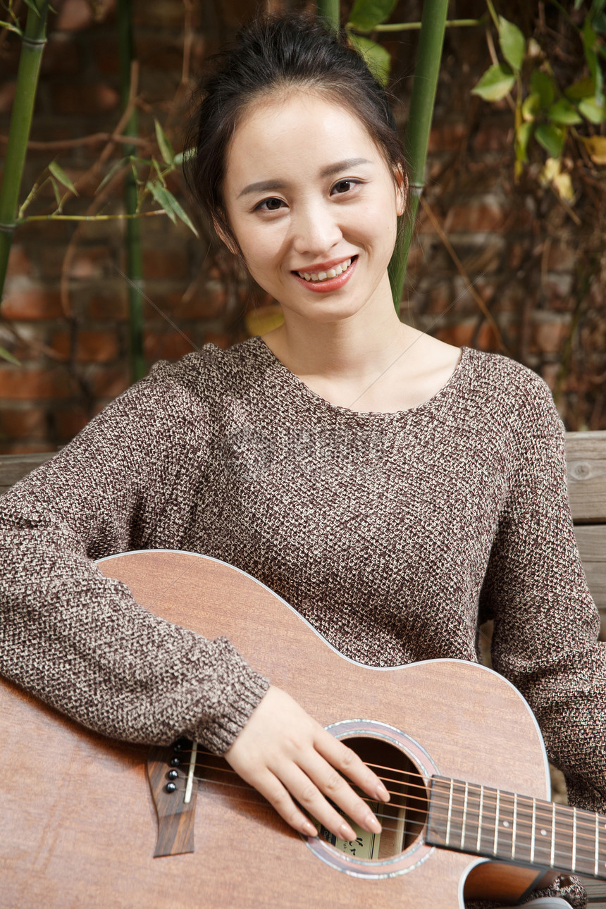 幸福亚洲高雅年轻女人弹吉他图片