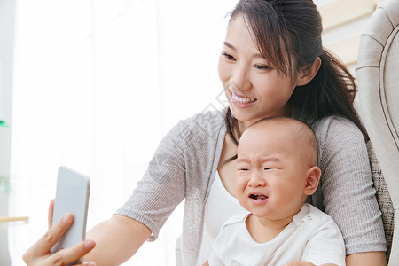 母婴亚洲人哭年轻妈妈和宝宝用手机照相图片