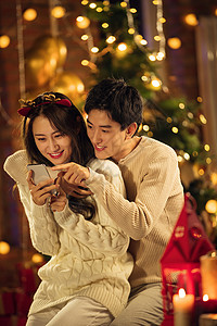 圣诞发卡青年男人女人微笑幸福的年轻伴侣在家玩手机背景