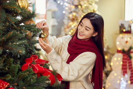 往圣诞树上挂装饰物的年轻女性背景图片