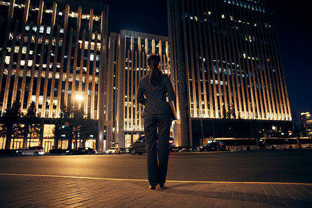 闹市区夜晚站在办公楼前的都市职场女性背影背景