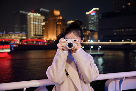 时尚美女服饰夜晚在游轮船上用相机拍照的旅游女生背景