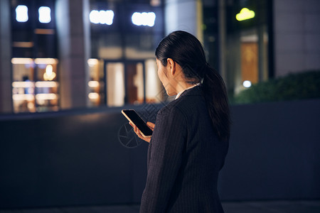 深夜站在写字楼外使用手机的女性背影高清图片