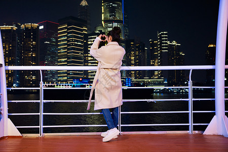 夜晚在游轮船上拍照打卡的旅游女生背影图片