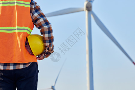 风力发电环保节能风车下男性工程师手拿安全帽特写背景