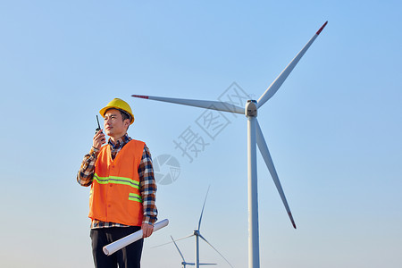 男性工程师在大风车下拿对讲机讲话图片