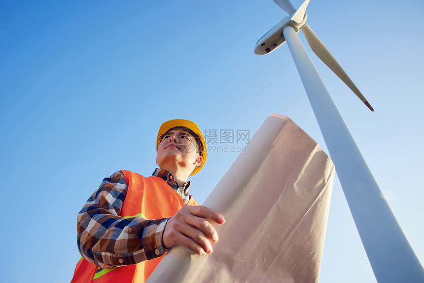 仰拍男性工程师在大风车下看图纸图片