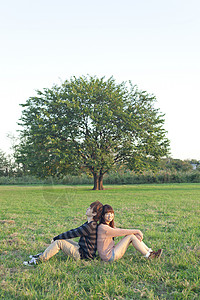 草地上背靠背坐着的情侣图片