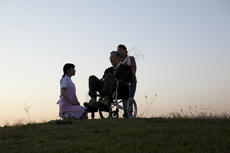 夕阳下照顾轮椅上老人的护理看护背景图片