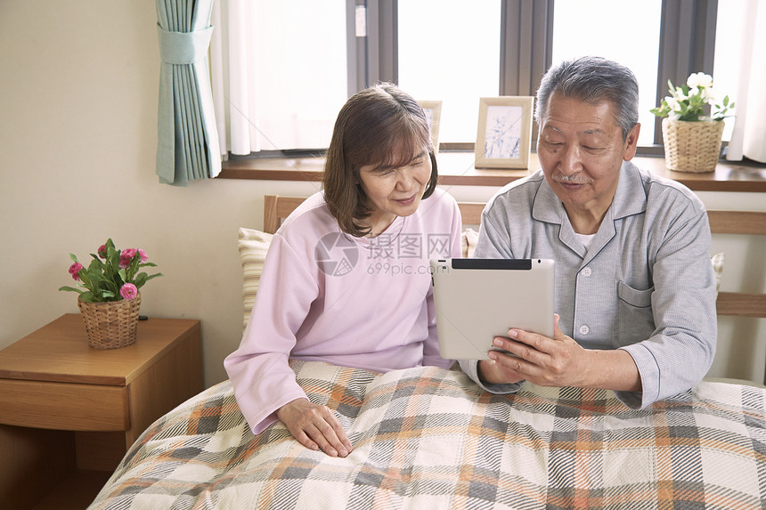 靠在床上看平板电脑的老年夫妇图片