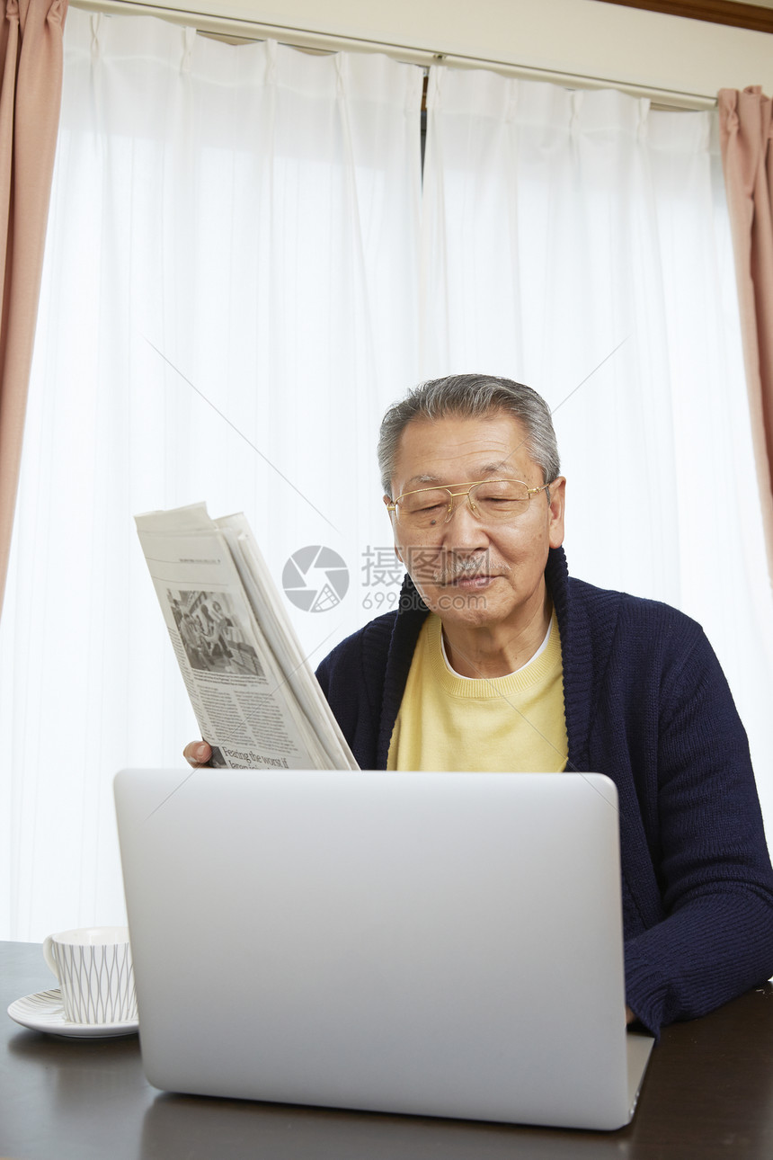 老年男性居家看报纸和电脑图片