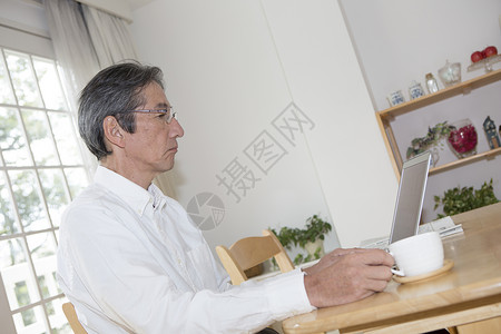 中年男性在桌子上看笔记本喝茶图片
