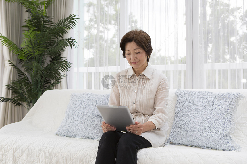 在沙发上使用平板电脑的中年女性图片