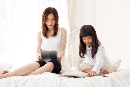 母亲跟女儿坐在床上看书背景图片