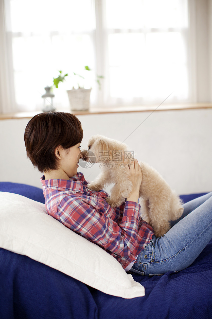 沙发上跟贵宾犬玩耍的妇女图片