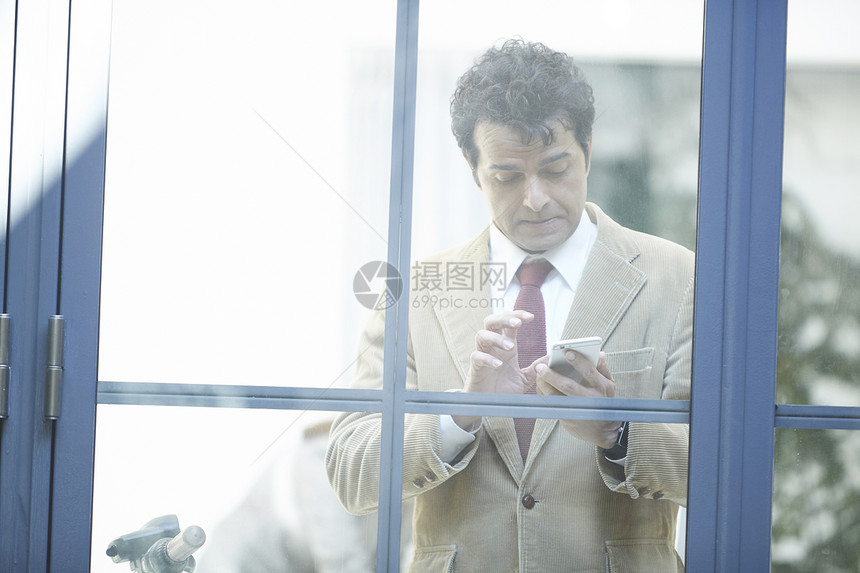 窗户外使用手机的商人图片