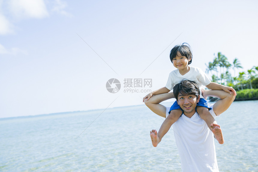 父亲背儿子沿着海滩散步图片