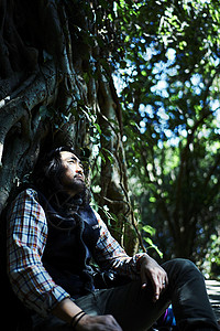 森林中冒险旅行的男背包客靠着树休息图片