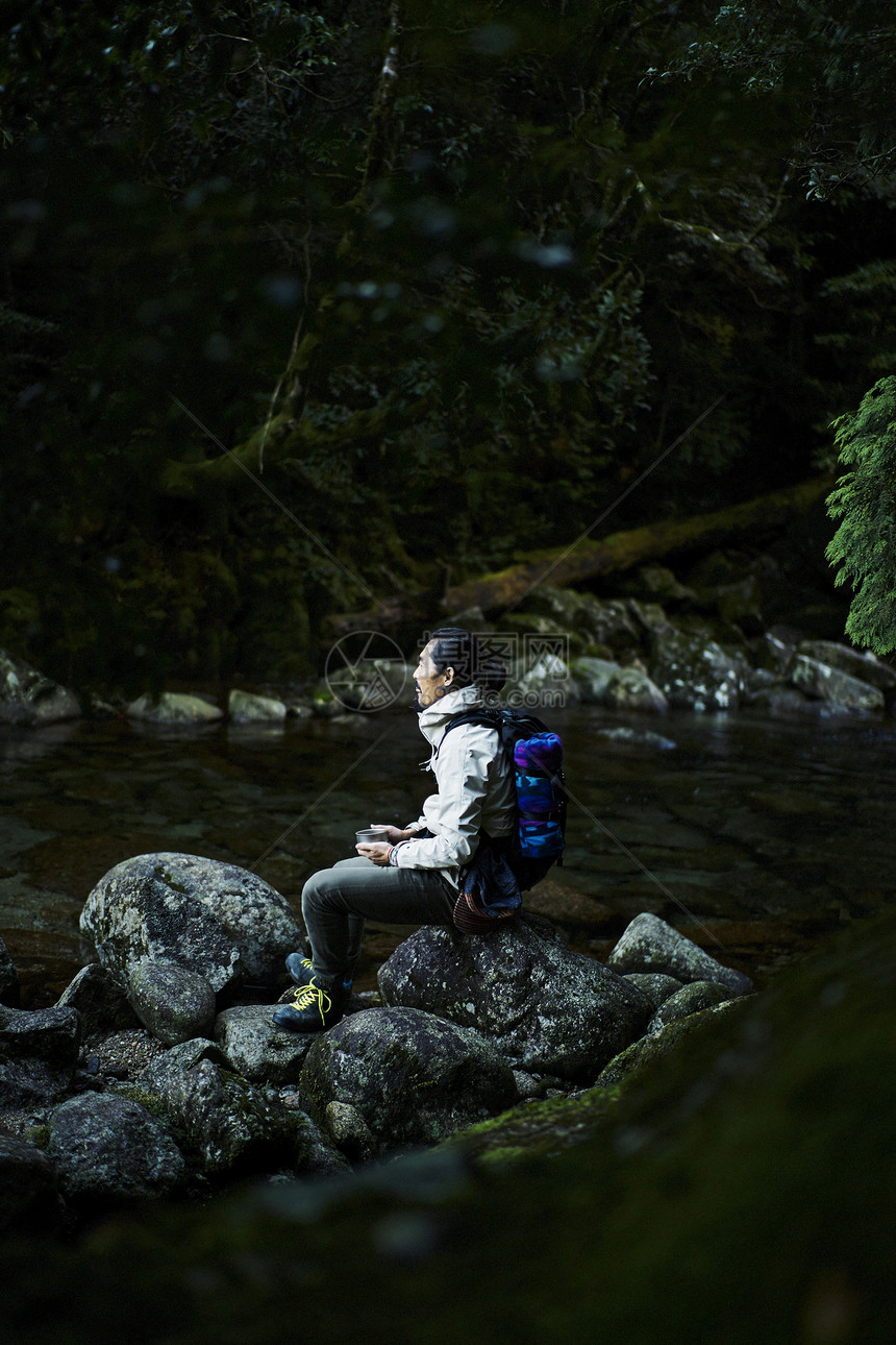 溪边喝水休息的男背包客图片