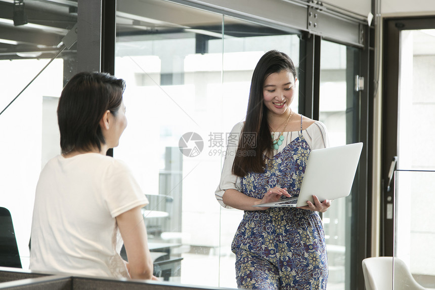 女人拿着笔记本电脑与同事讨论图片