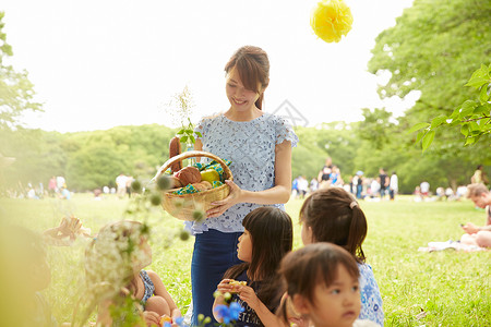 在公园微笑拿着午餐看向孩子们的女人图片