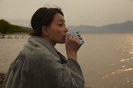 夕阳下在海边举起杯子喝水的女性图片