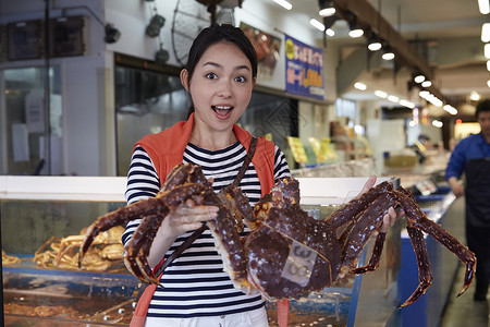 在市场上拿着螃蟹正对镜头的女生图片
