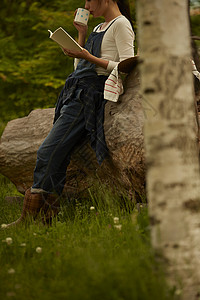 靠在树旁喝茶看书的农业女孩画像图片