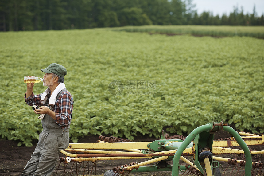老人在田地边靠着农具休息喝水图片
