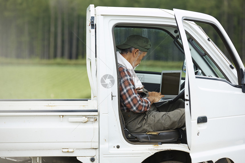 老人坐在农用轻卡车上用笔记本电脑图片