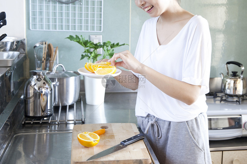 在厨房切橙子的女性图片