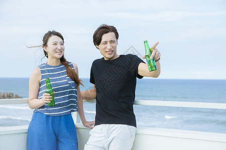 海边喝啤酒聊天的青年父亲户外高清图片素材