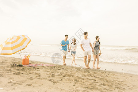 明亮的太阳伞下走在海滩上快乐男人和女人图片