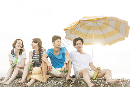 明亮的太阳伞下享受海滩的快乐男人和女人好朋友高清图片素材