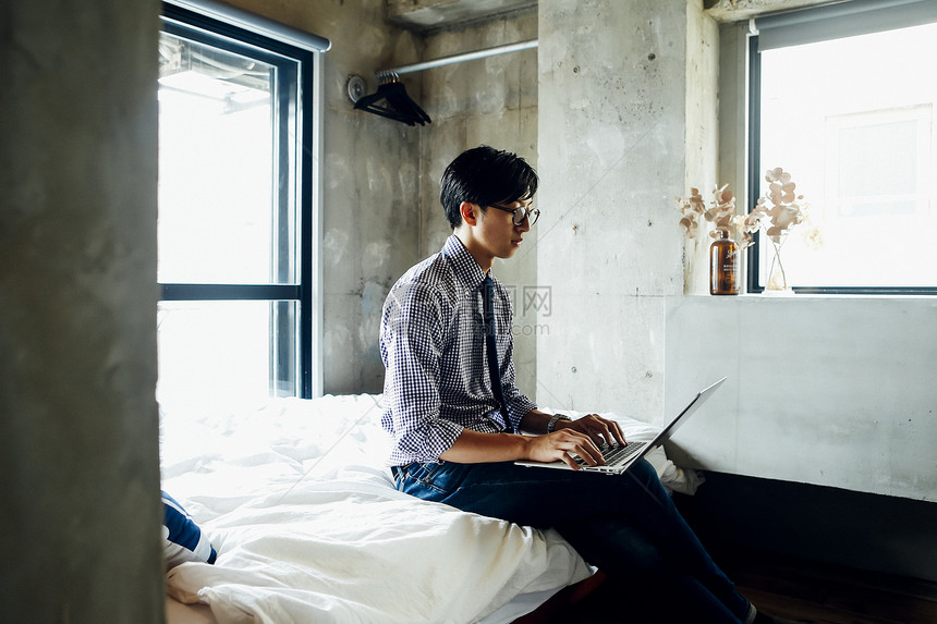 坐在床上使用笔记本电脑的男子图片