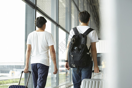 两个男人拖着行李箱走在机场大厅背影图片