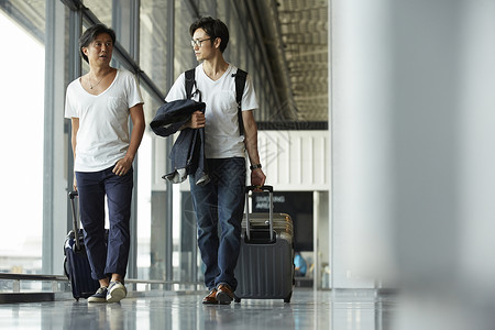 两个男人拖着行李箱走在机场大厅图片