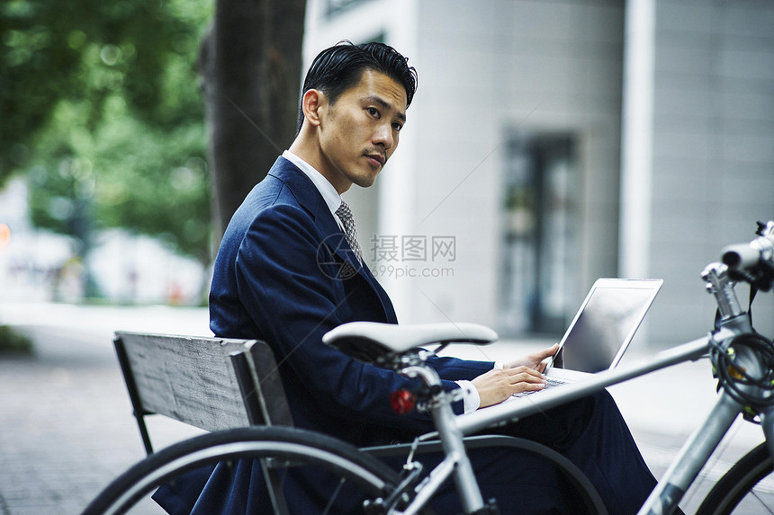坐在长椅子上使用笔记本电脑的男人图片