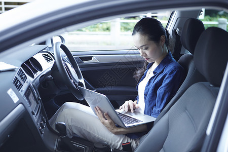 在汽车驾驶位上用笔记本电脑工作的年轻女性图片