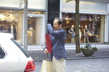 在街上拿着手提袋准备开后备箱的年长男性图片